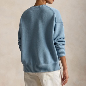 Model wearing Polo Ralph Lauren knitwear in Blue Note, back view, with ribbed hem and cuffs, styled with cream trousers.