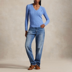 Model wearing blue cable-knit V-neck sweater with embroidered logo, styled with light-wash straight-leg jeans and brown loafers.