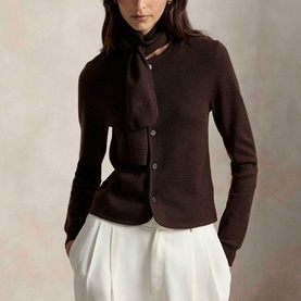 Model wearing Polo Ralph Lauren Deep Chocolate Melange knit cardigan with scarf tie neck detail, styled with white wide-leg trousers.