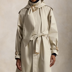 Model wearing Polo Ralph Lauren Buckled Scarf Hooded Trench Coat in Classic Stone with belted scarf neckline and brass buckle self-belt.