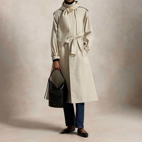 Model wearing Polo Ralph Lauren Buckled Scarf Hooded Trench Coat in Classic Stone with self-belt, styled with blue jeans and black loafers, carrying