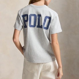 Model wearing Polo Ralph Lauren Grey Ash Heather T-Shirt, back view showing large navy POLO logo graphic, styled with cream trousers.