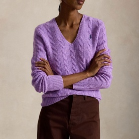 Model wearing Polo Ralph Lauren cable-knit V-neck sweater in Amethyst Falls Heather, styled with dark brown trousers, arms crossed.