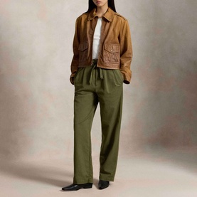 Model wearing Polo Ralph Lauren Belted Pleated High-Rise Straight Leg Trousers in olive, styled with a tan leather jacket and white top.