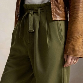 Model wearing Polo Ralph Lauren Belted Pleated High-Rise Straight Leg Trousers in olive, styled with a tan leather jacket.