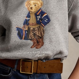 Model wearing Polo Ralph Lauren Dark Vintage Heather sweat top with Polo Bear graphic, styled with blue jeans and tan leather belt.
