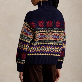 Model wearing navy Fair Isle turtleneck knit jumper with red, yellow and purple snowflake pattern, styled with brown trousers