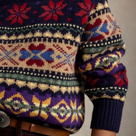 Model wearing a Fair Isle knit jumper in navy, purple, red and cream multicolour pattern, styled with a brown belt.