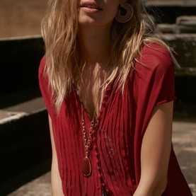 Model wearing red pintuck V-neck blouse, styled with gold pendant necklace and hoop earrings