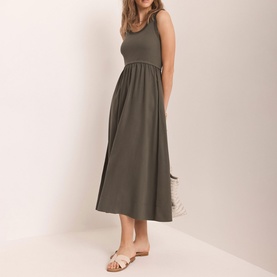 Model wearing Mint Velvet green sleeveless midi dress with gathered waist and full skirt, styled with white flat sandals