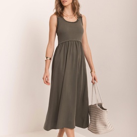 Model wearing Mint Velvet green sleeveless midi dress with gathered waist, styled with a striped tote bag and gold bracelet.