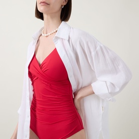Model wearing Sea Level Cross Front Swimsuit in red with gathered V-neckline, styled with a white oversized shirt and pearl necklace.