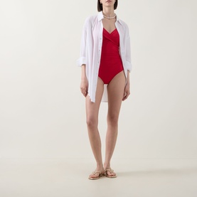 Model wearing Sea Level Cross Front Swimsuit in red with V-neckline and gathered cross front, styled with white shirt and tan sandals.