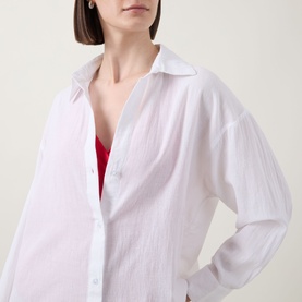 Model wearing Sea Level Vacay Cruise Shirt in white cotton, semi-sheer with point collar and long sleeves, styled over a red top.