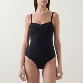 Model wearing Sea Level black swimsuit with twist-front bandeau neckline and thin straps, styled with a pearl necklace.