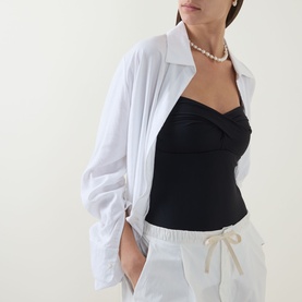 Model wearing Sea Level black swimsuit styled with a white oversized shirt and cream drawstring trousers, pearl necklace