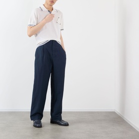 Model wearing Jacquemus dark navy casual trousers with a white polo shirt and black loafers.