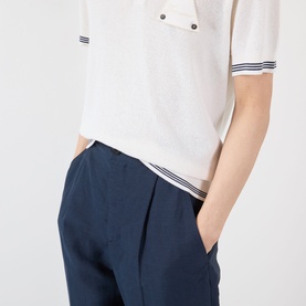 Model wearing Jacquemus dark navy casual trousers with front pleats and side pockets, styled with a white polo shirt with stripe trim.