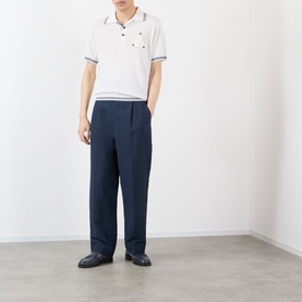 Model wearing Jacquemus dark navy casual trousers with wide-leg fit, styled with a white polo shirt and dark loafers.