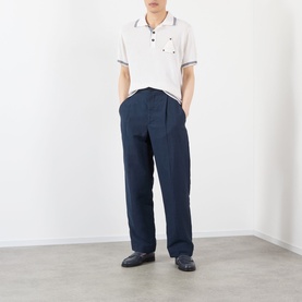 Model wearing Jacquemus white polo with navy tipped collar, styled with navy wide-leg trousers and dark loafers