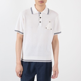 Model wearing Jacquemus white polo shirt with navy tipped collar, cuffs and hem, chest pocket, and short sleeves, styled with navy trousers