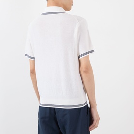 Model wearing Jacquemus white polo shirt, back view, with navy tipping detail on collar and cuffs, styled with navy trousers
