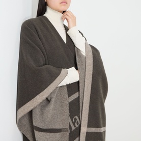 Model wearing Max Mara Accessories Hilde Logo Fringed Cape in dark brown with bold logo detail, styled over a white turtleneck
