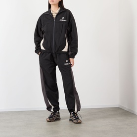 Model wearing Pellador OG Logo Track Jacket in black with contrast panels, styled with matching black track pants and chunky trainers.