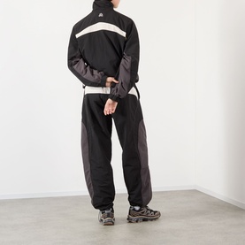 Model wearing Pellador OG Logo Track Jacket in black with contrast panels, paired with matching black track pants and grey trail shoes.