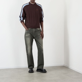 Model wearing Pellador Overlap Cable Knit Sweater in brown with blue stripe sleeves, styled with khaki jeans and black loafers.
