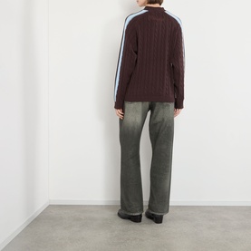 Model wearing Pellador Overlap Cable Knit Sweater in brown with light blue double-stripe sleeves, styled with grey washed jeans. Rear view.