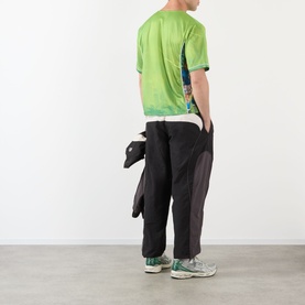 Model wearing Pellador Logo Football T-Shirt in green with black trousers and green trainers, shot from behind