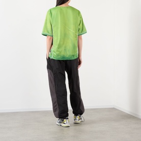 Model wearing Pellador Logo Football T-Shirt in green jersey style, paired with dark joggers and chunky trainers, back view.