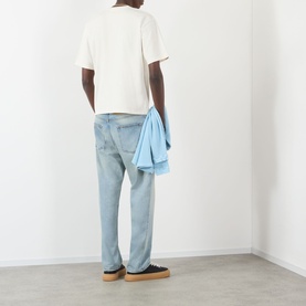 Model wearing Pellador Red Setter Logo T-Shirt in white, seen from behind, styled with light blue jeans and a denim shirt draped over arm.