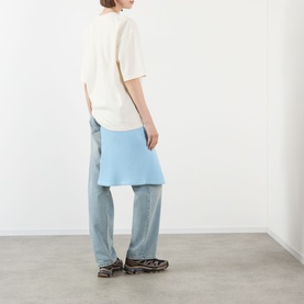 Model wearing Pellador Red Setter Logo T-Shirt in white with light blue knit skirt and wide-leg jeans, shot from behind.