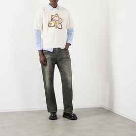 Model wearing Pellador Swan Logo T-Shirt in white with logo graphic, layered over blue shirt, styled with dark wash jeans and black loafers.
