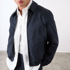 Model wearing A.P.C. dark navy cotton casual jacket, open over a white shirt, with ribbed cuffs and collar detail.
