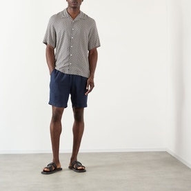 Model wearing A.P.C. Bennet Printed Shirt in dark navy, camp collar, short sleeves, styled with navy shorts and brown sandals.
