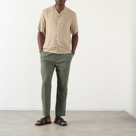 Model wearing A.P.C. beige short-sleeve camp collar shirt in viscose, styled with olive green trousers and brown leather sandals.