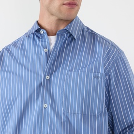 Model wearing A.P.C. blue grey striped cotton casual shirt with chest pocket, styled over a white crew-neck tee.