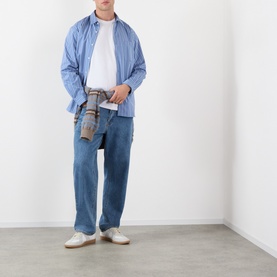 Model wearing A.P.C. blue grey cotton casual shirt, styled with mid-wash jeans and white trainers, holding a small bag.