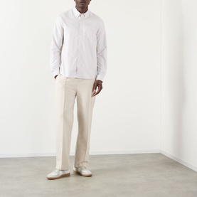 Model wearing A.P.C. beige cotton casual shirt with button-down collar, styled with cream tailored trousers and silver loafers