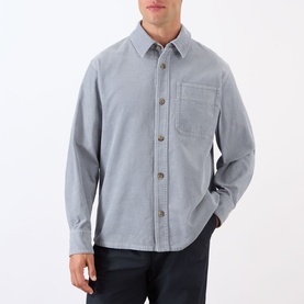 Model wearing A.P.C. blue grey cotton casual shirt with chest pocket and button-front, styled with dark navy trousers.