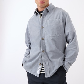 Model wearing A.P.C. blue grey cotton casual shirt with chest pocket, styled with a striped crew-neck top and navy trousers.