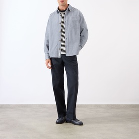 Model wearing A.P.C. blue grey cotton casual shirt, styled with striped T-shirt and dark straight-leg trousers.