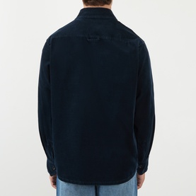 Model wearing A.P.C. Patch Pocket Corduroy Shirt in dark navy, rear view, showing dropped shoulders and curved hem, styled with blue jeans.