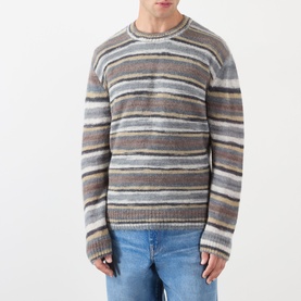 Model wearing A.P.C. grey striped mohair-alpaca crew neck jumper with multicolour horizontal stripes, styled with light blue jeans.