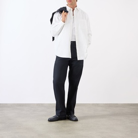 Model wearing A.P.C. dark navy cotton jeans with a white shirt and black loafers, jacket draped over shoulder.