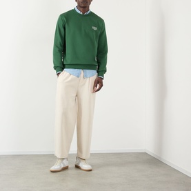 Model wearing A.P.C. dark green cotton sweatshirt with small logo, styled with cream trousers and light blue shirt.