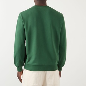 Model wearing A.P.C. dark green cotton sweatshirt, back view, with cream trousers.